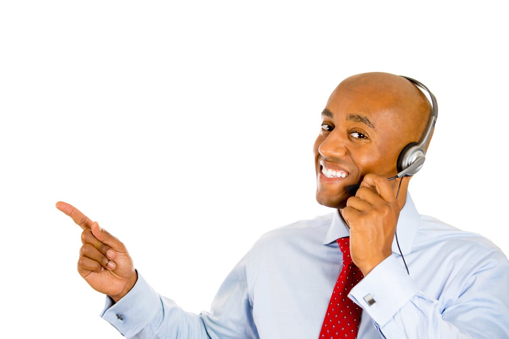 Closeup portrait of a young male customer service representative or call centre worker or operator or support staff speaking with head set, isolated on white background and pointing to copy space